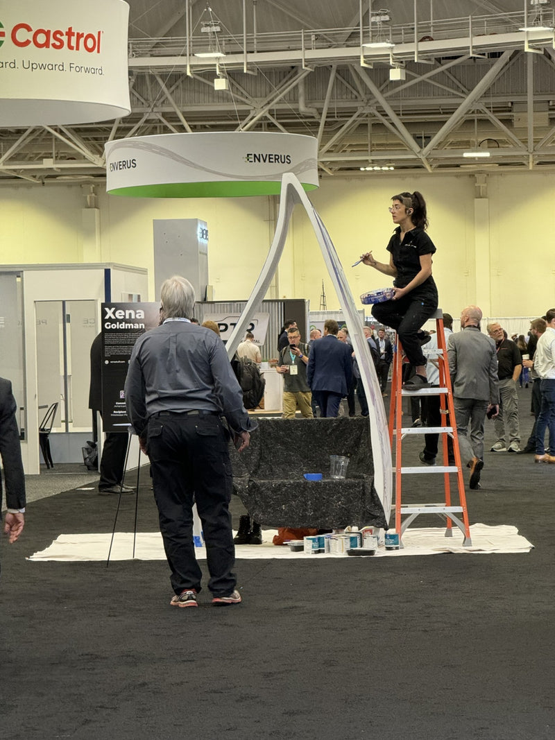 Live public art demonstration featuring an artist painting a Noblewins bench made from a recycled wind turbine blade at an industry trade show