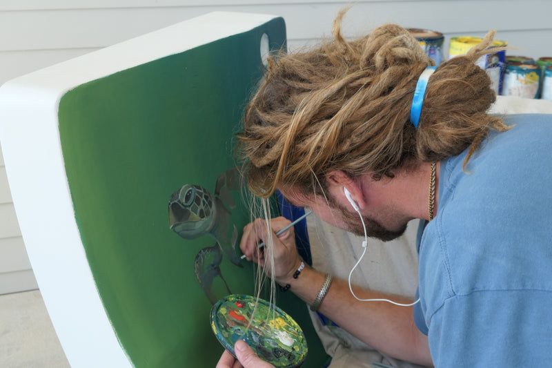Artist painting a sea turtle mural on a bench made from a repurposed wind turbine blade